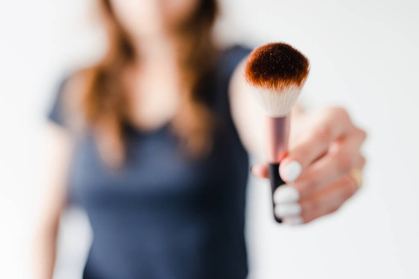 girl holding make-up brushes in front of the camera showing the product shot at shallow depth of field, concept of beauty bloggers and influencers recommanding products or making online make-up tutorials,  - Photo, Image