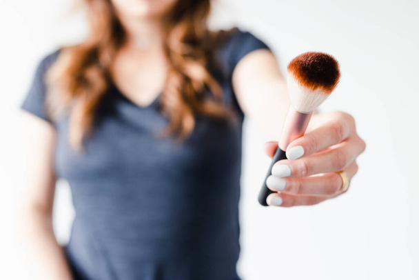 girl holding make-up brushes in front of the camera showing the product shot at shallow depth of field, concept of beauty bloggers and influencers recommanding products or making online make-up tutorials,  - 写真・画像