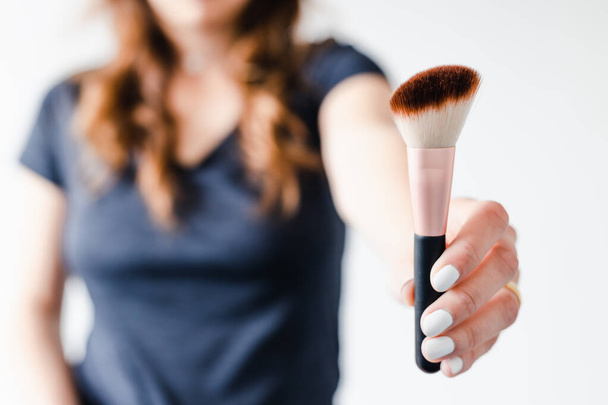girl holding make-up brushes in front of the camera showing the product shot at shallow depth of field, concept of beauty bloggers and influencers recommanding products or making online make-up tutorials,  - Фото, изображение