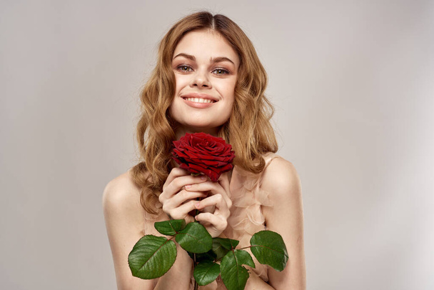 Κοκκινομάλλα γυναίκα με ένα τριαντάφυλλο στα χέρια της σε ένα ελαφρύ φόντο συναισθήματα μοντέλο πορτρέτο γκρο πλαν - Φωτογραφία, εικόνα