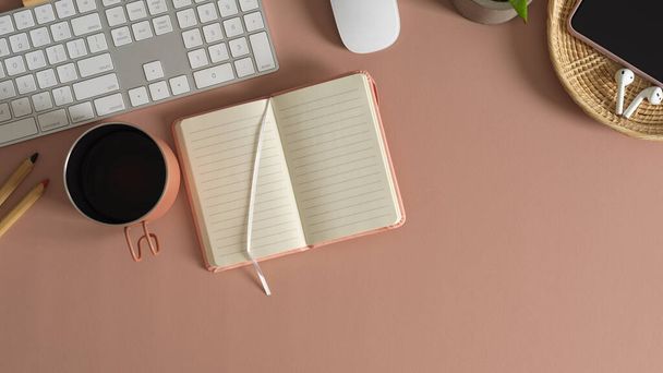 Bovenaanzicht van moderne werktafel met blanco notitieboek, koffiebeker en kantoorbenodigdheden op roze tafelachtergrond - Foto, afbeelding