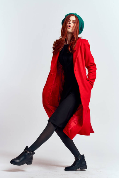 emocjonalna kobieta w czerwonym płaszczu i kapeluszu w pełnym wzroście na jasnym tle czarne buty stanowią model - Zdjęcie, obraz