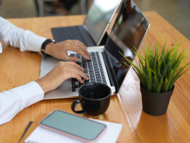 Vue latérale des mains féminines travaillant avec un ordinateur portable, une tablette, un smartphone et des documents sur un bureau en bois - Photo, image