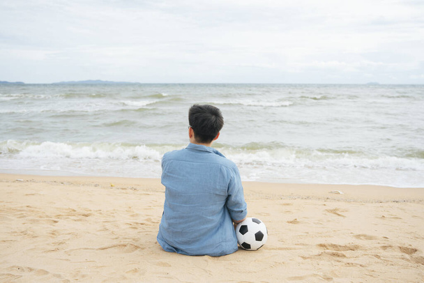 Back view - Retired football player sitting on beach with a ball. - Foto, immagini
