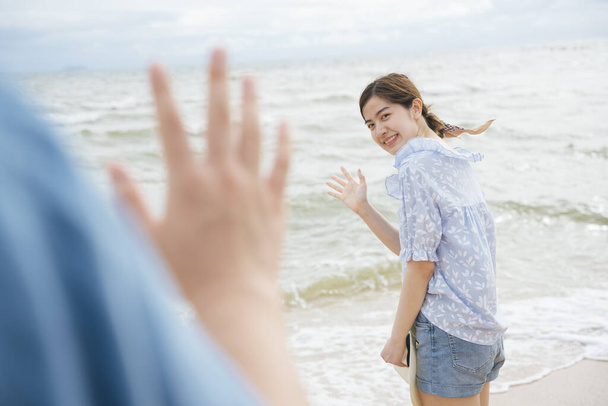 Красивая азиатка машет рукой, чтобы поздороваться с незнакомцем на пляже.. - Фото, изображение