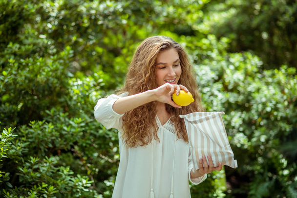 Long -haired woman in white shirt putting a lemon into a bag - Foto, imagen