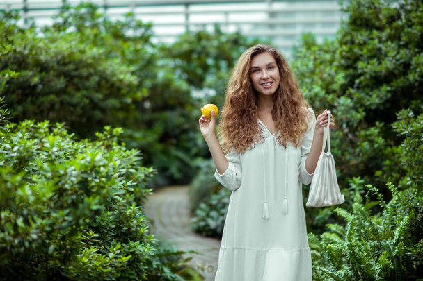Cute woman in white dress holding a lemon and smiling - Foto, Imagen