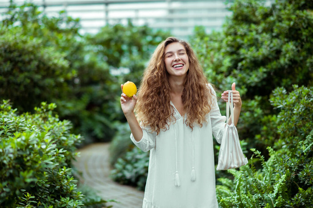 Woman in white dress holding a lemon and looking happy - Фото, зображення