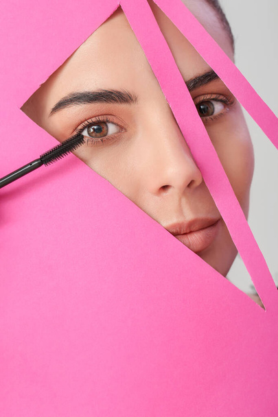 Beautiful young woman with mascara visible through cut color paper - Photo, Image