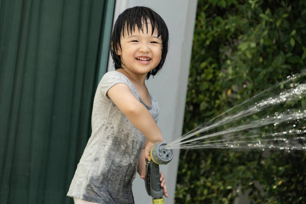 3 yaşındaki Asyalı bir çocuğun bahçe hortumuyla su oynadığı komik bir an. Çocukların yaz ve oyun zamanı için arka plan kavramı. - Fotoğraf, Görsel