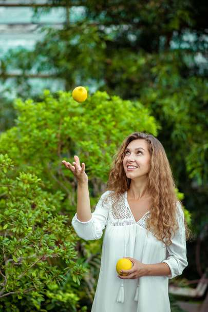 Woman in white dress standing near the tree and throwing a lemon - Foto, Imagem