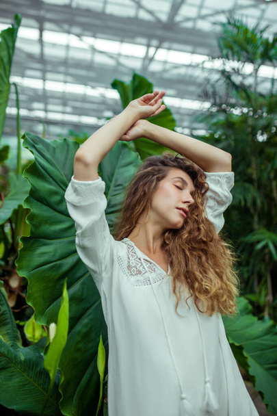Woman in white dress standing in the greenhouse and looking relaxed - Foto, Bild
