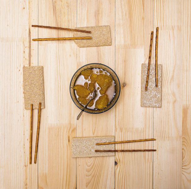 Een kopje met bijenhoning, broden en rietjes liggen op een houten tafel - Foto, afbeelding