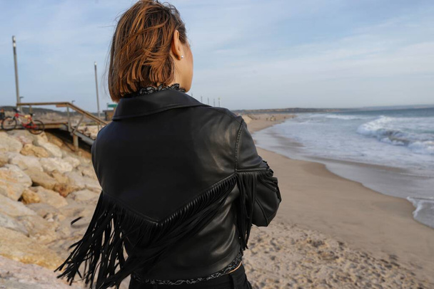 Schöne kaukasische Frau am Strand von Costa da Caparica in der Nähe des Stadtzentrums von Lissabon. Schöne junge Frau mit Lederjacke entspannt am Strand bei Sonnenuntergang in Caparica. Portugal, 2020 - Foto, Bild