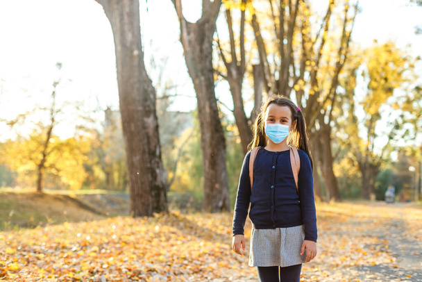 Petite fille portant un masque médical pour prévenir la pollution sur les feuilles tombées au parc. - Photo, image