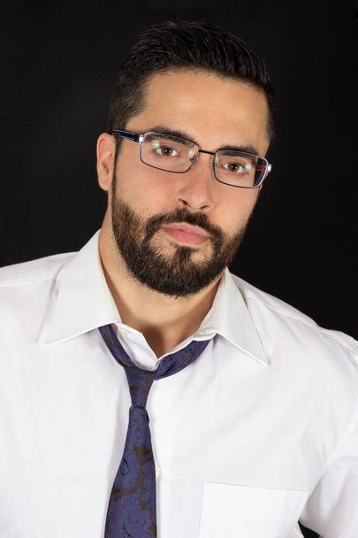 Portrait of handsome young bearded man with glasses in formal wear. Optical male model. Attractive stylish businessman with tie and shirt. Black background. - Foto, imagen