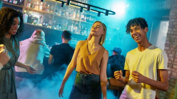 Attractive caucasian young woman and mixed race guy having fun, dancing with friends at party in the bar - Foto, afbeelding