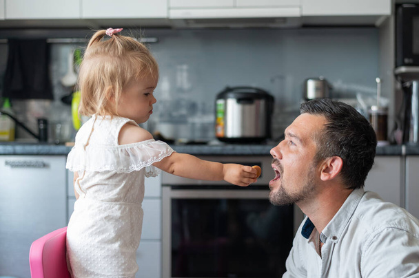 Cute little girl is feeding her dad in the kitchen - Zdjęcie, obraz