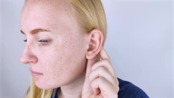 Una mujer sobre un fondo blanco muestra su oreja. El macro video muestra el rizo de la aurícula, que tiene un tubérculo. Concepto de cirugía plástica - Metraje, vídeo