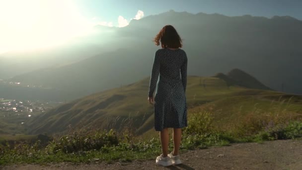 Nuori nainen seisoo mekossa ja nostaa kätensä ylös katsellen vuoria. Hidastus. - Materiaali, video