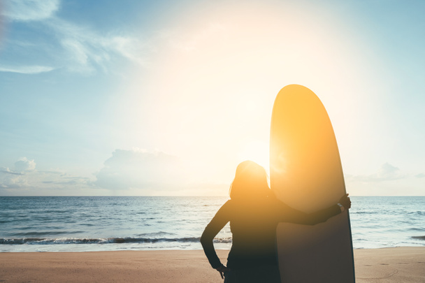 Nő tartja szörfdeszka álló trópusi naplemente strand háttér. Nyári vakáció és sport adventrue koncepció. Vintage hangszűrő hatás színes stílus. - Fotó, kép