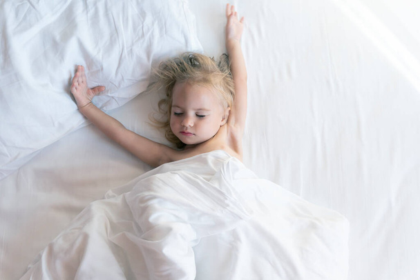 Widok z góry na cute dość kaukaskie dziecko śpi w łóżku z białą pościelą - Zdjęcie, obraz
