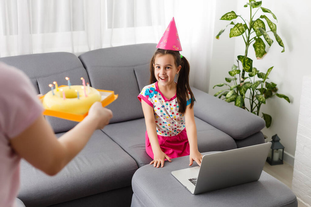 Lapset virtuaalinen syntymäpäiväjuhlat kakku verkossa yhdessä hänen ystävänsä videoneuvottelussa. Digitaalinen puhelin verkkotapaamiseen. Tyttö juhlii syntymäpäivää verkossa karanteeniaikaan - Valokuva, kuva