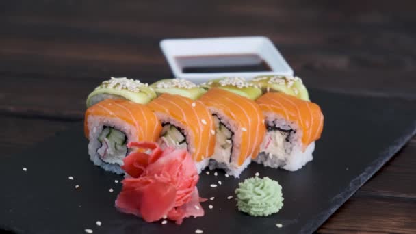 Set de rollos de sushi con atún, salmón, pepino, aguacate espolvorear con semillas de sésamo sobre fondo negro de cerca. Surtido de comida japonesa en restaurante. - Metraje, vídeo