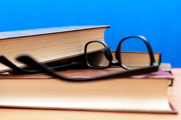 Könyvek és szemüvegek egy fa asztalon, kék trendi puha háttér - Fotó, kép
