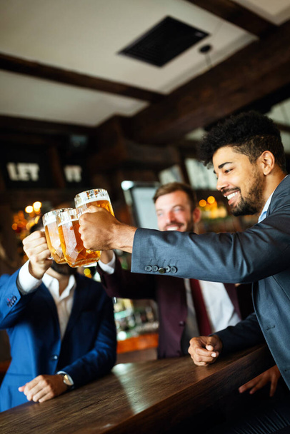 People, men, leisure, friendship and celebration concept. Happy business male friends drinking beer at pub - Fotó, kép