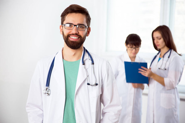 Portrait of a young doctor in a clinic with colleagues on the background - Foto, Imagen