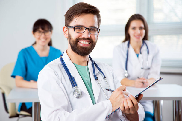 Portrait of a young doctor in a clinic with colleagues on the background - Photo, image