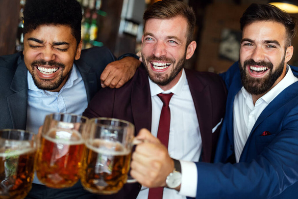 Handsome young businessmen drinking beer, talking and smiling while resting at the pub - Φωτογραφία, εικόνα