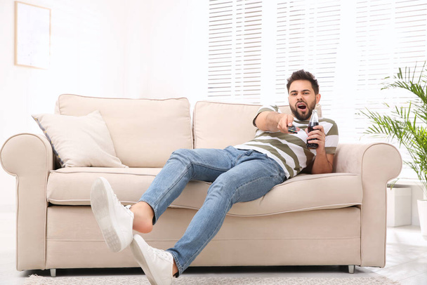 Lazy young man watching TV on sofa at home - Foto, Imagem
