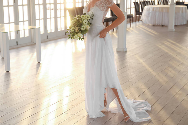Bride in beautiful wedding dress with bouquet in restaurant, closeup - Фото, изображение