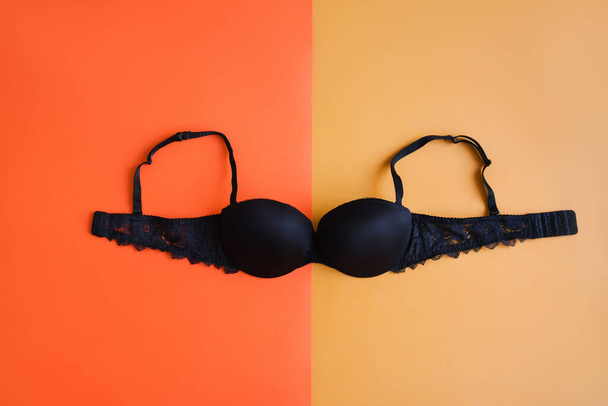 Black bra on background of orange and yellow color, top view. Women's lingerie - Foto, afbeelding