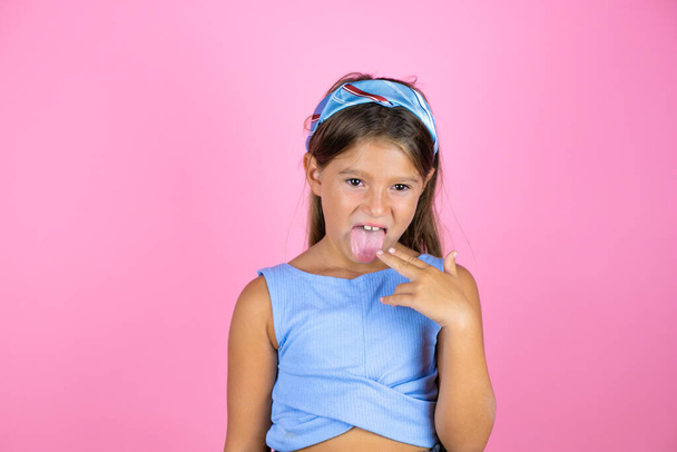 Jeune belle enfant fille sur fond rose isolé dégoûté avec sa main à l'intérieur de sa bouche - Photo, image