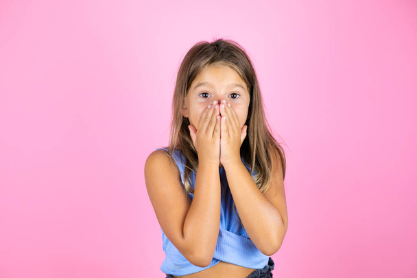 Joven niña hermosa sobre fondo rosa aislado con las manos sobre la boca y sorprendida - Foto, Imagen