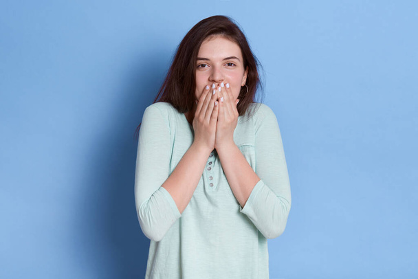 Astonished young female covering mouth with hands, her eyes full of surprise and shock, winsome lady in light blue casual shirt, looks ant camera, expressing positive. - 写真・画像