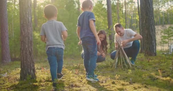 Family sits around a campfire on a summer evening. Children with their parents are resting in the woods. Weekend in nature in good company. Family frying sausages over a fire in the woods. - Footage, Video