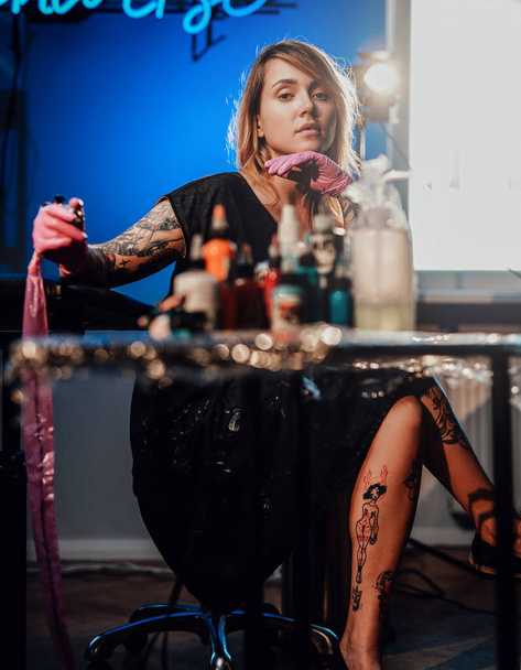 Tattoo meester zitten op stoel en poseren in haar kleine salon - Foto, afbeelding