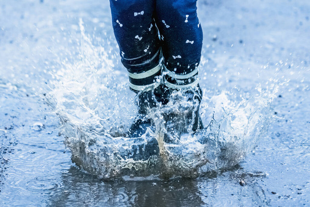 Herfst regenachtig weer. Kind in regenlaarzen springend en spetterend in plassen na regen.  - Foto, afbeelding