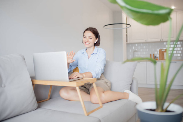 Office work home concept. Happy young woman teacher in headphones greets in video chat with laptop students - Photo, Image