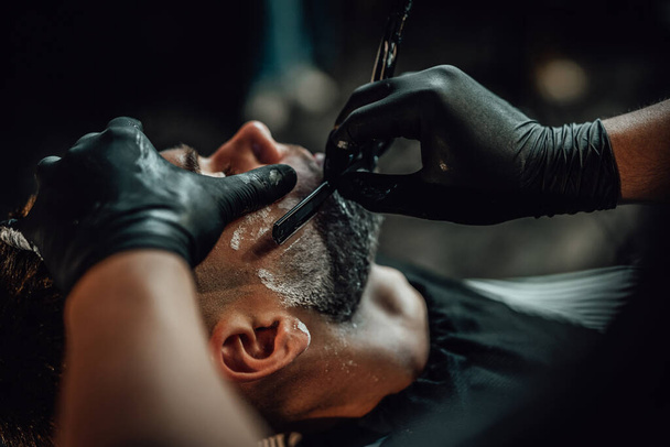 Skillful barber shaving a customers beard in saloon - 写真・画像