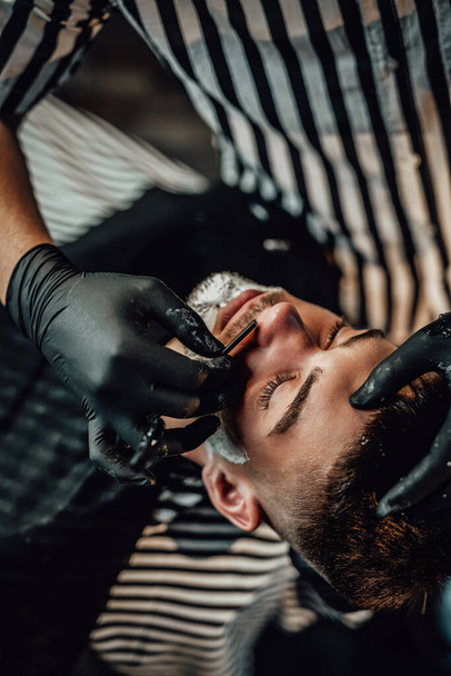 Skillful barber shaving a customers beard in saloon - Foto, Imagem