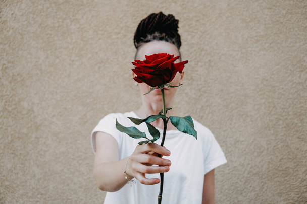 Flower Power, Zeichen des Friedens, Ende der Gewalt, Symbol des friedlichen Protests. Eine rote Rose in weiblicher Hand auf weißem Hintergrund. - Foto, Bild