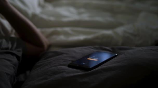 Close up of alarm clock on a digital cell phone display waking up a man in bed. Concept. Sleepy man turning off alarm clock and continuing sleeping in his cozy bed at home. - Footage, Video