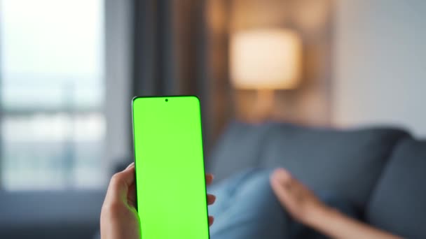 Woman at home lying on a sofa and using smartphone with green mock-up screen in vertical mode. Girl browsing Internet, watching content, videos, blogs. POV. - Séquence, vidéo