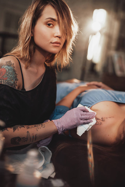 Τατουάζ master με τον πελάτη της σε λαμπερό και φωτεινό στούντιο - Φωτογραφία, εικόνα