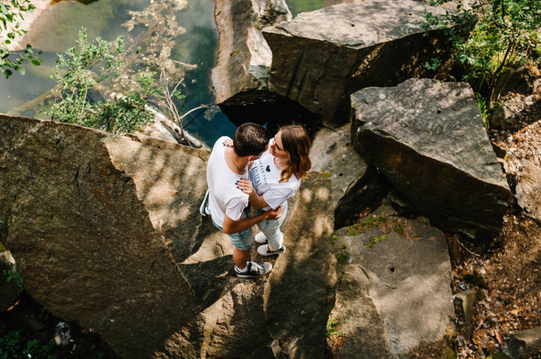 Junges Paar umarmt einen Stein in der Nähe des Sees. Ein Mann und eine Frau stehen vor dem Hintergrund der Felsen. Ansicht von oben. Die Natur. Herbst. in voller Länge. Sich anschauen. - Foto, Bild